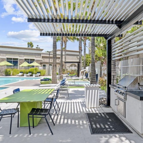 a grill area with tables and chairs near a swimming pool